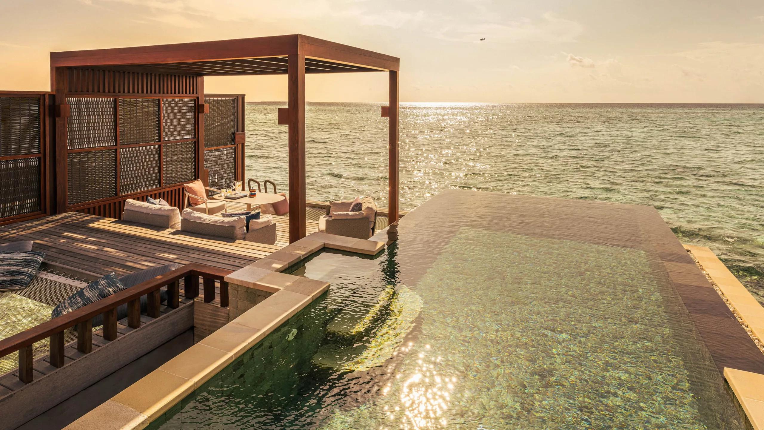 The plunge pool and deck of a Sunset Water Villa, open directly onto the ocean at sunset