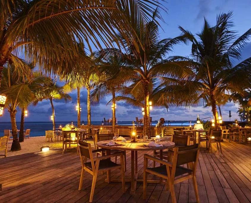 Sangu Restaurant's candlelit terrace tables under palm trees at dusk, ocean beyond