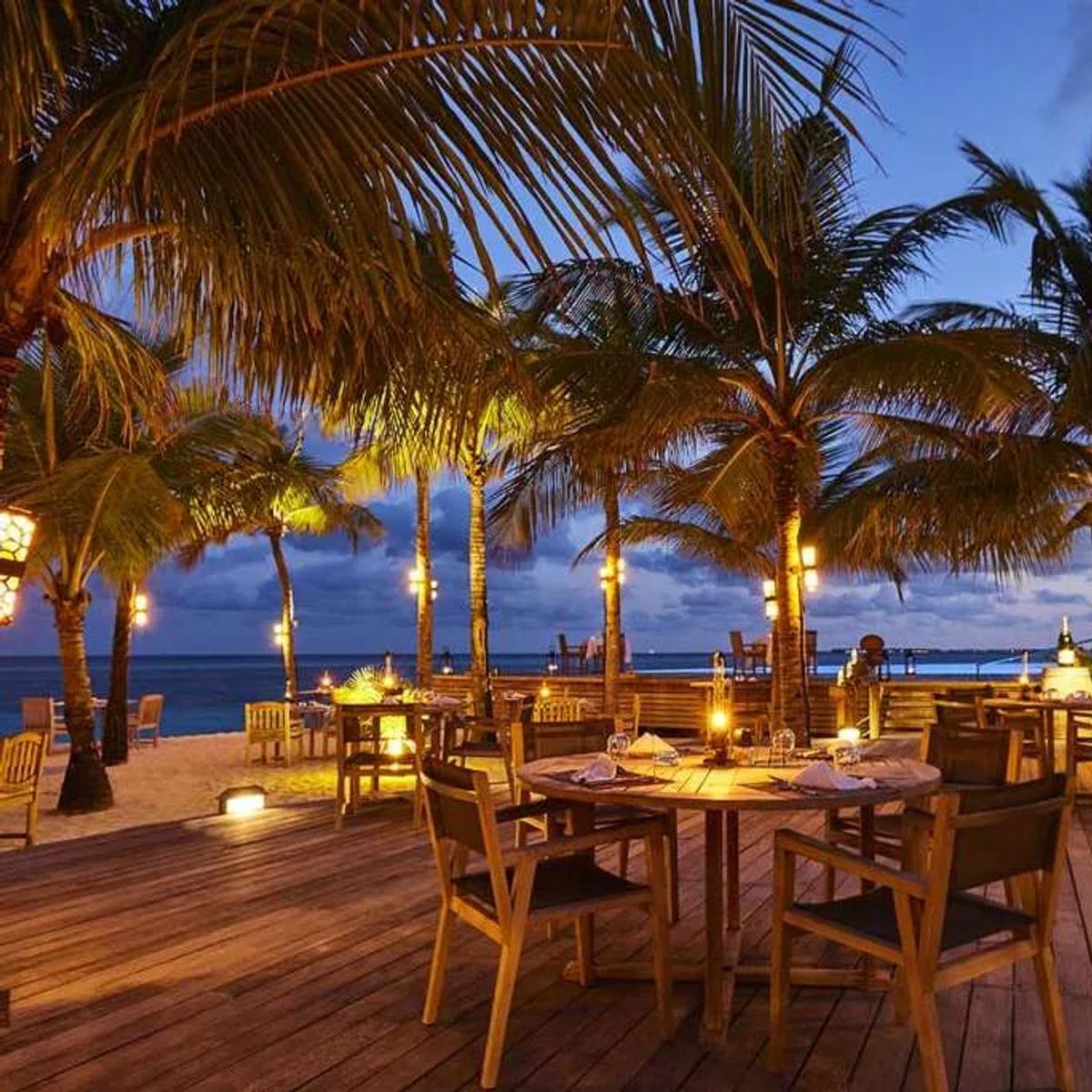 Sangu Restaurant's candlelit terrace tables under palm trees at dusk, ocean beyond