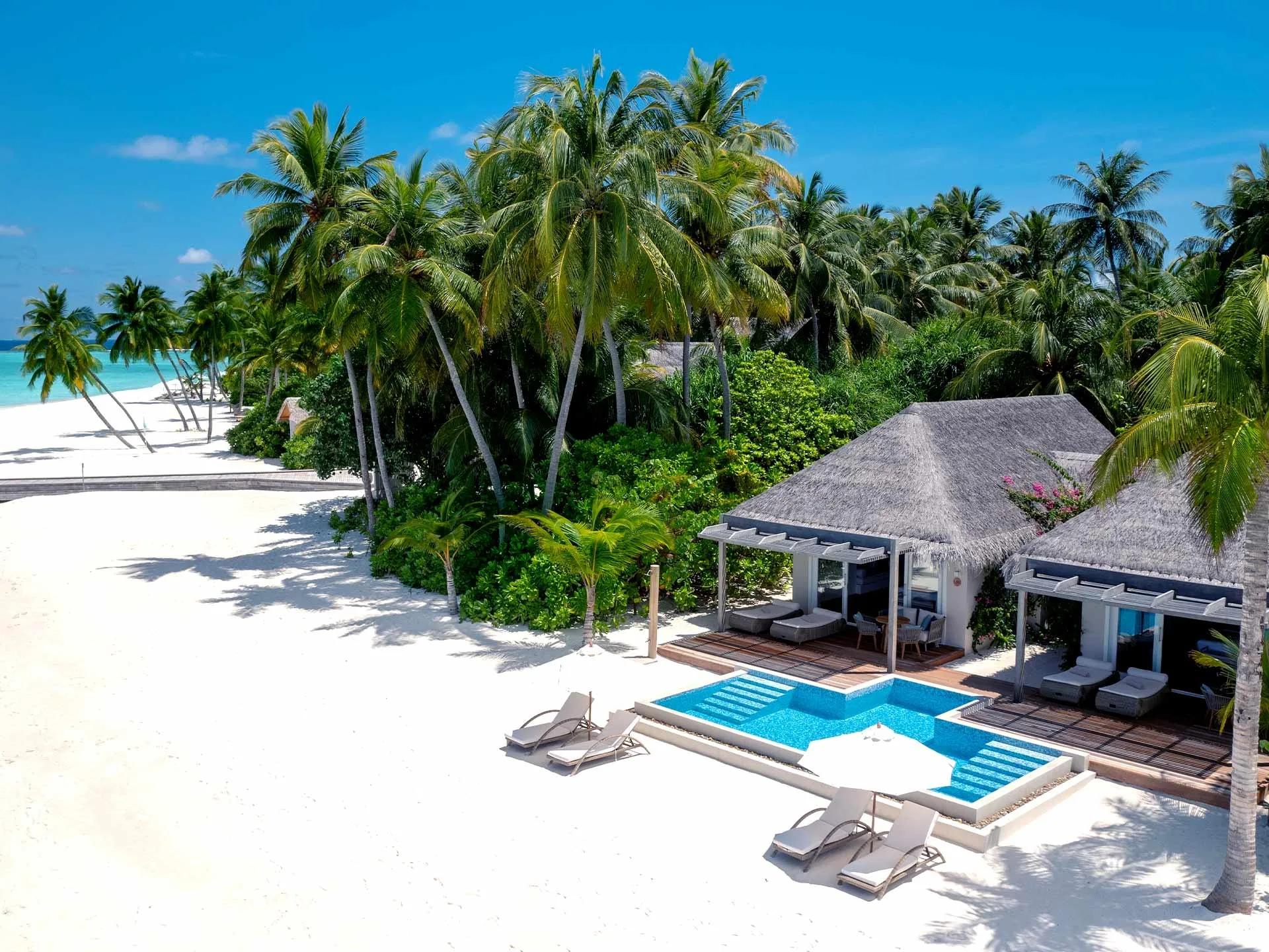 A Two-Bedroom Family Beach Villa with Pool seen from the beach, its private pool and thatched pavilions set among palm trees
