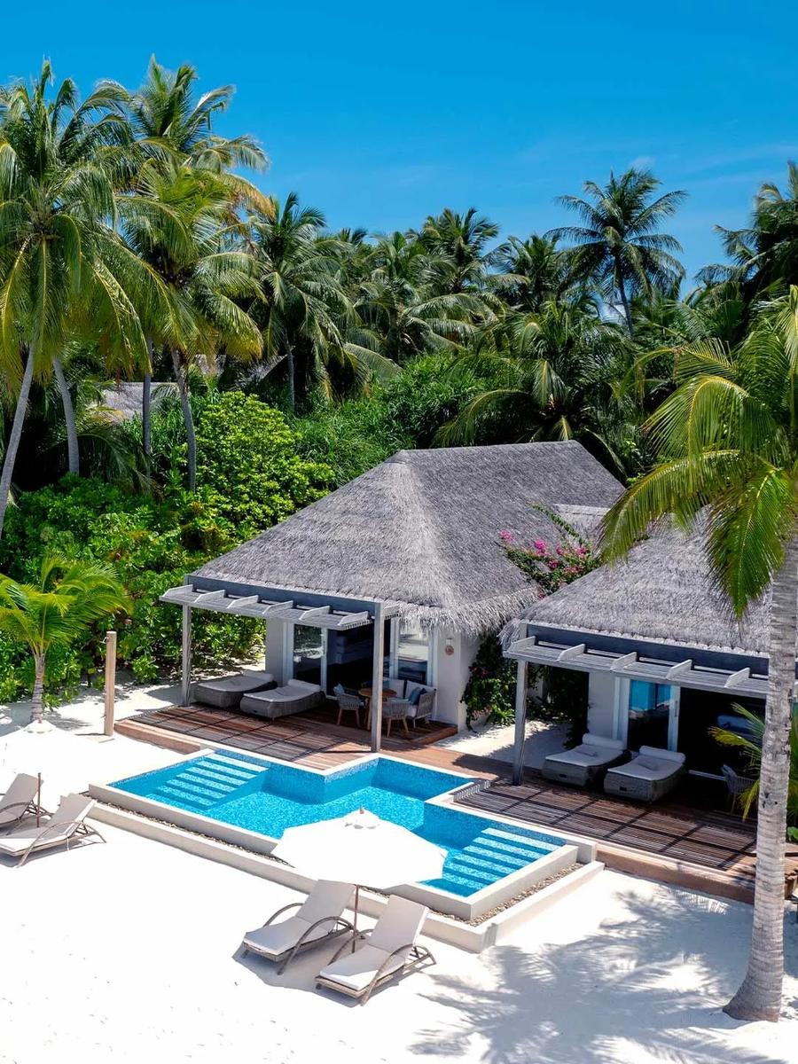 A Two-Bedroom Family Beach Villa with Pool seen from the beach, its private pool and thatched pavilions set among palm trees