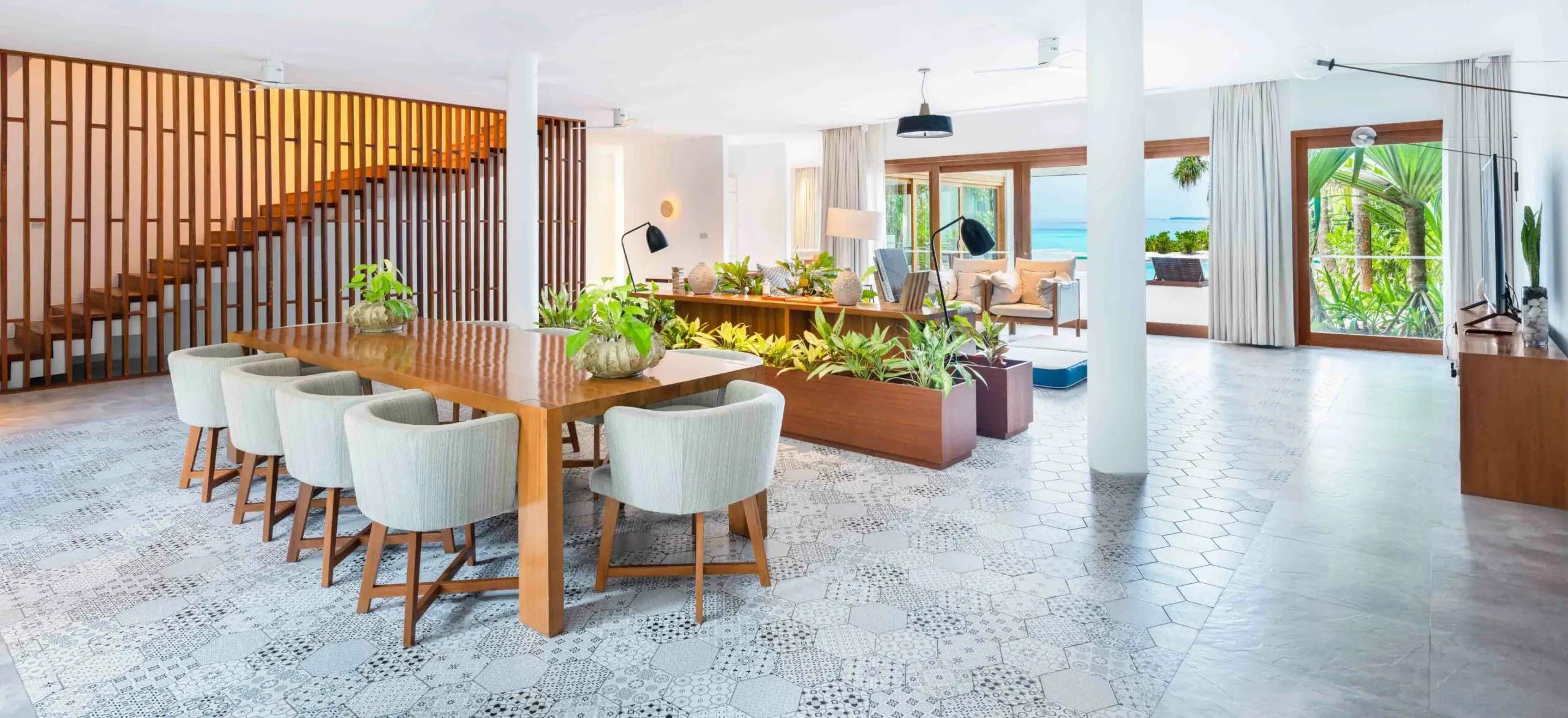 The dining and living area of a Four-Bedroom Beach Residence at Amilla, with the pool and ocean visible through the windows