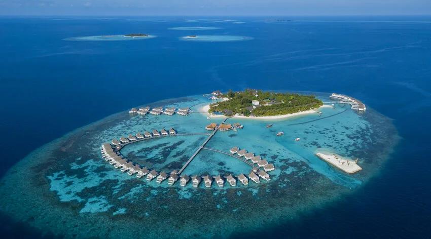 Aerial view of the full island, overwater villas ringing the reef edge with open ocean beyond