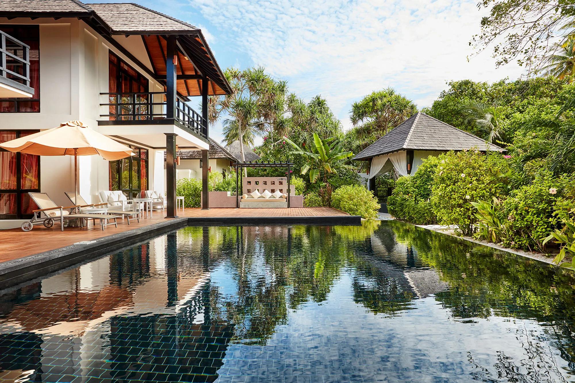 A balcony corridor overlooking a rooftop plunge pool and outdoor dining table at the Celebrity Retreat, garden and neighbouring rooftops beyond