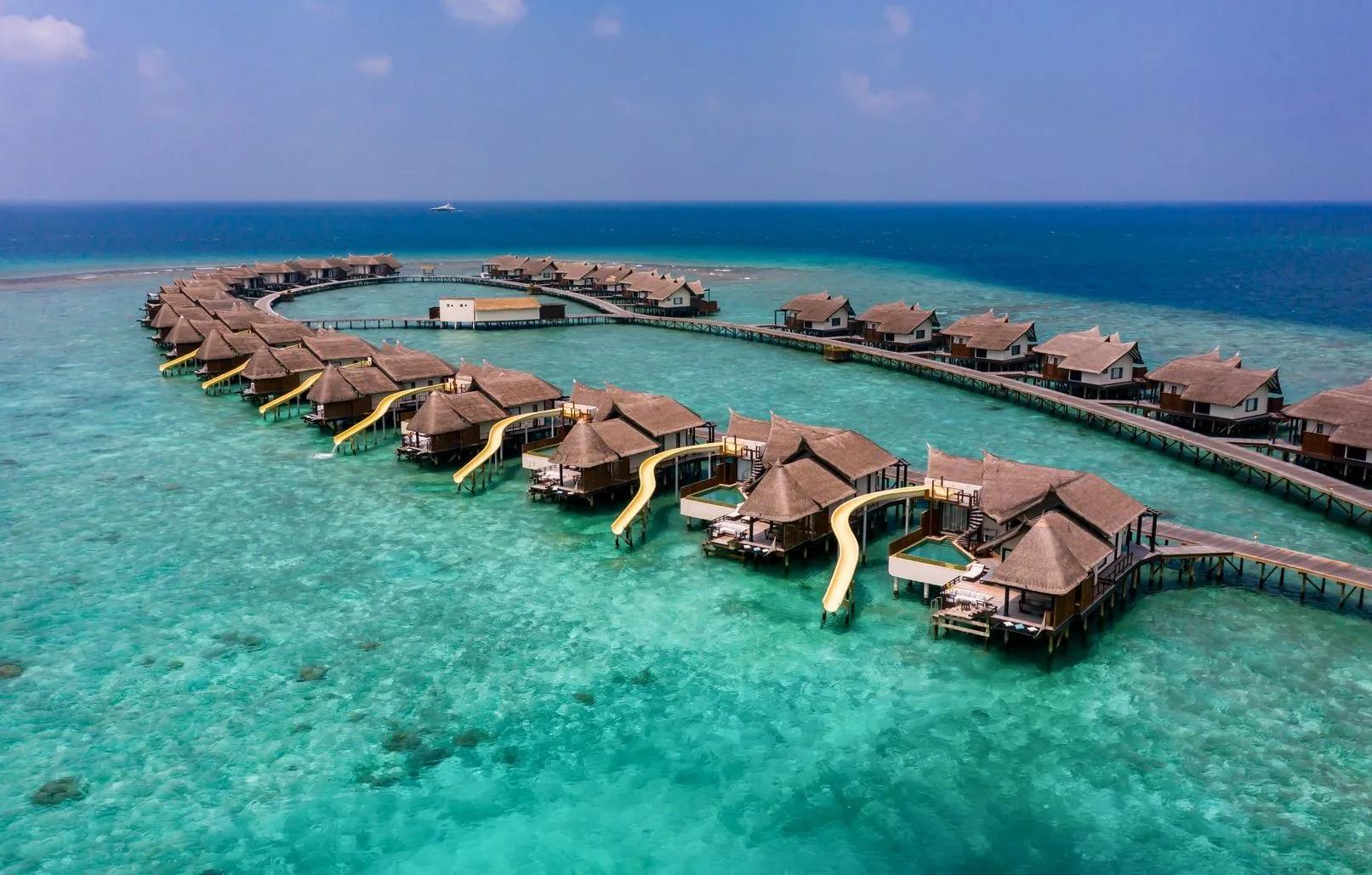 Aerial view of OZEN Reserve Bolifushi's overwater villas curving into the lagoon, each with a yellow slide running from the deck into the water