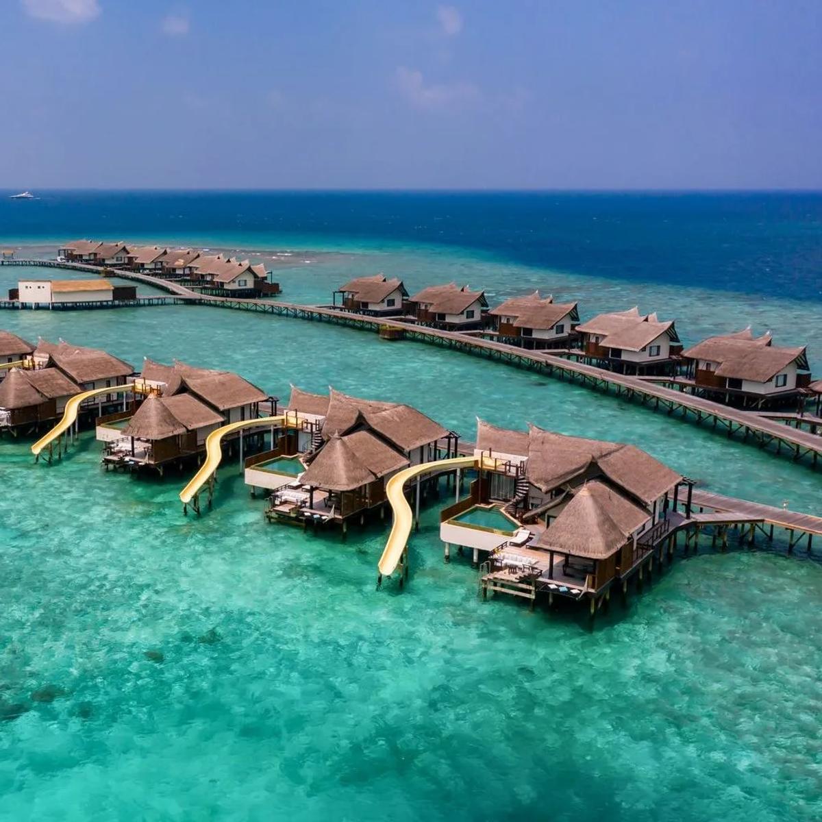 Aerial view of OZEN Reserve Bolifushi's overwater villas curving into the lagoon, each with a yellow slide running from the deck into the water