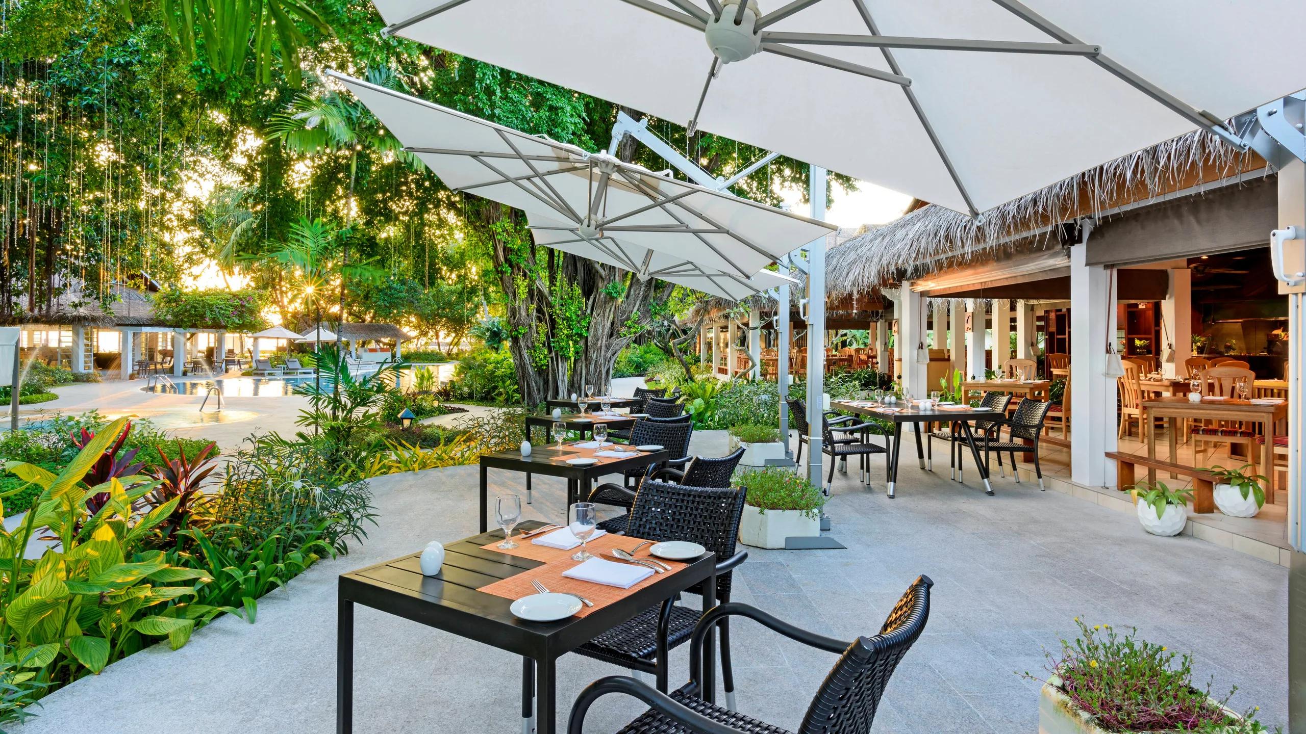 Feast's garden terrace set with dinner tables at dusk, string lights overhead and the pool visible nearby