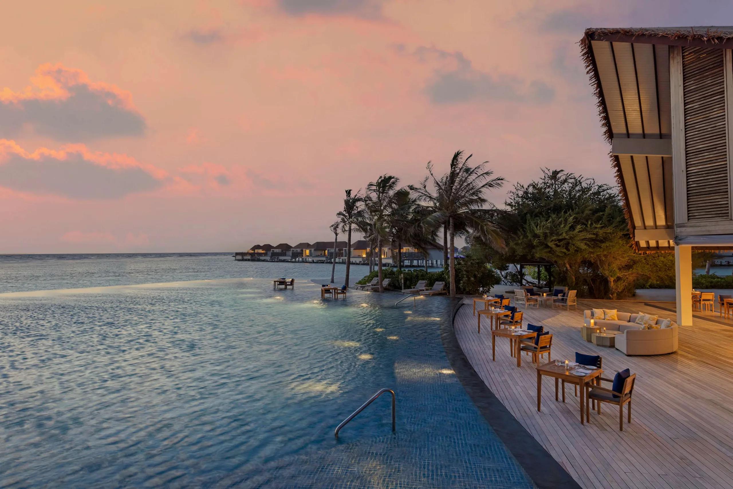 A sunset view along the pool deck toward the villas at Radisson Blu Resort Maldives; a dedicated photograph of Crusoe's Beach Bar was not available in this research pool, so this poolside deck image stands in