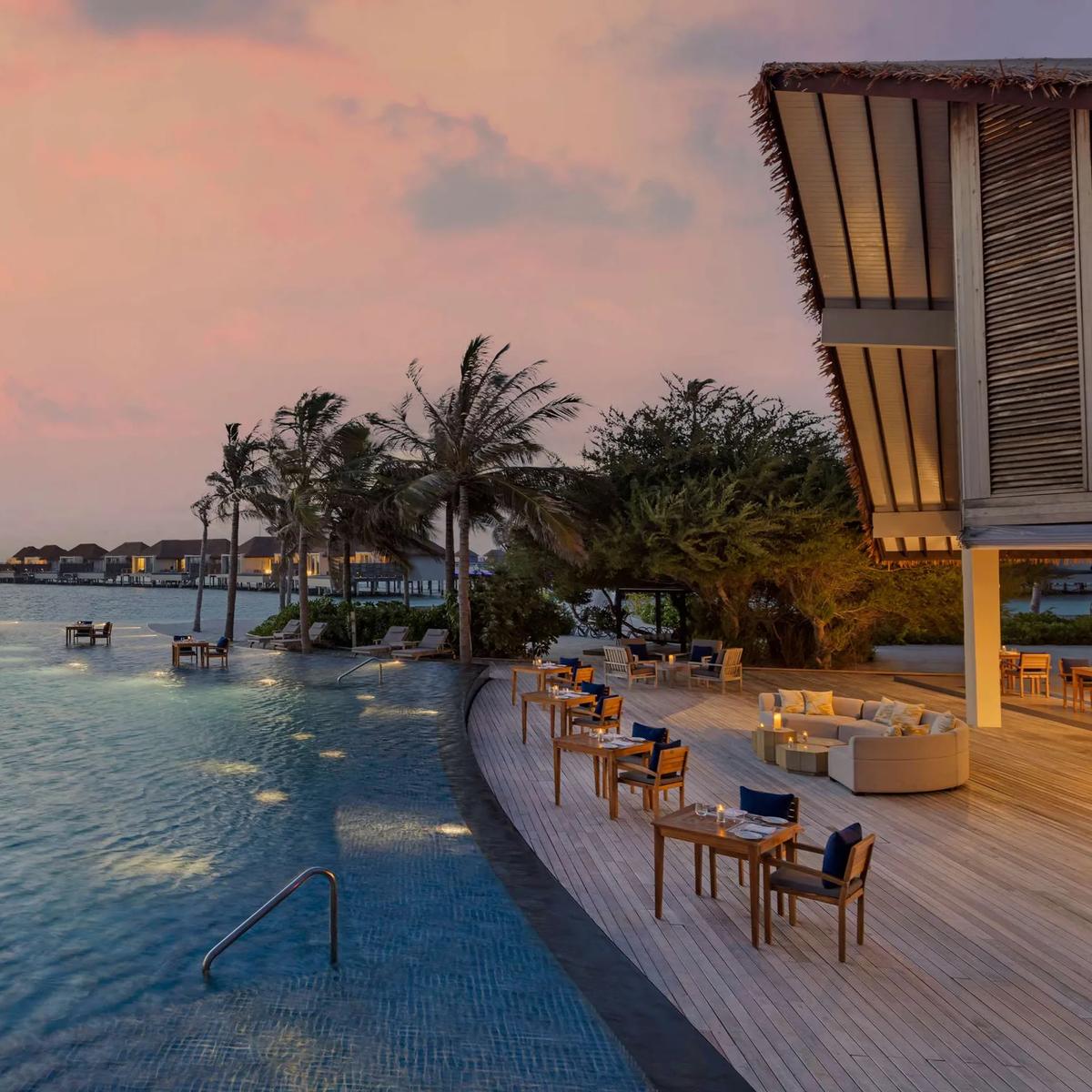A sunset view along the pool deck toward the villas at Radisson Blu Resort Maldives; a dedicated photograph of Crusoe's Beach Bar was not available in this research pool, so this poolside deck image stands in