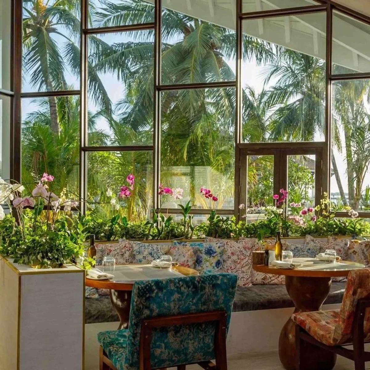 An orchid-lined dining nook at Vista del Mar, with floor-to-ceiling windows onto the palm garden