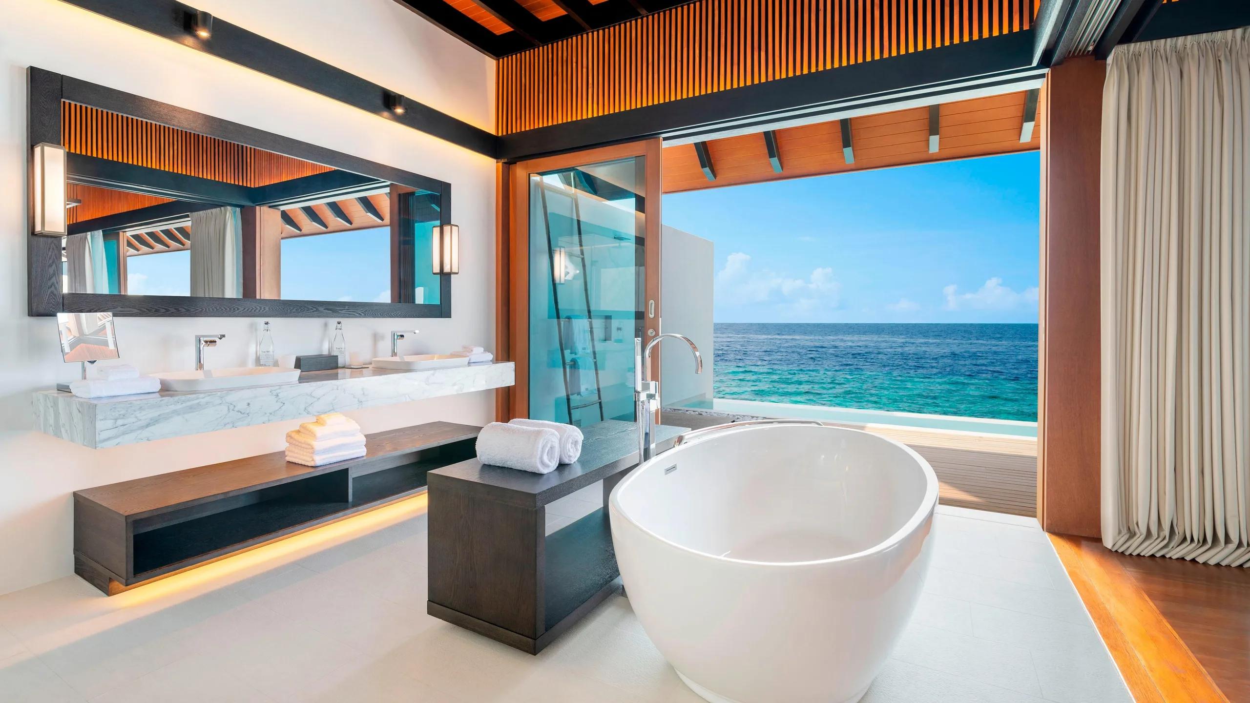 A Heavenly Overwater Villa bathroom with a freestanding tub, glass walls open to the reef