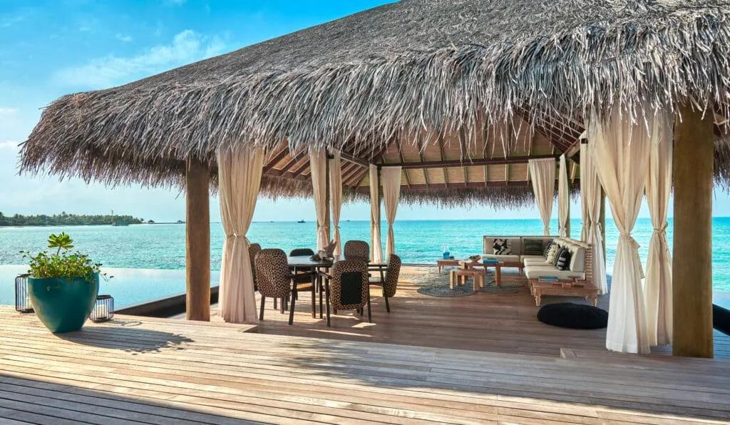 Overwater deck of a multi-bedroom water villa, with lounge seating, curtains and open ocean views