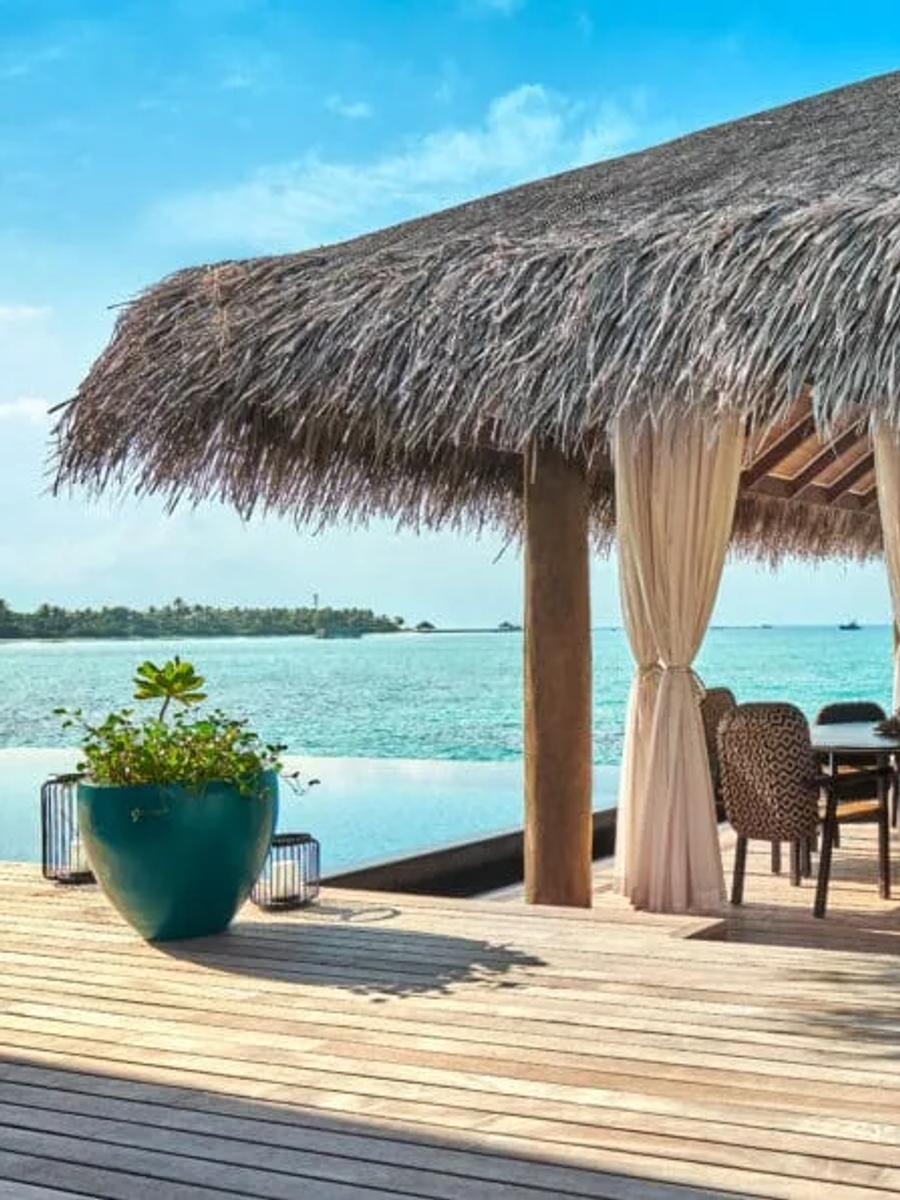 Overwater deck of a multi-bedroom water villa, with lounge seating, curtains and open ocean views