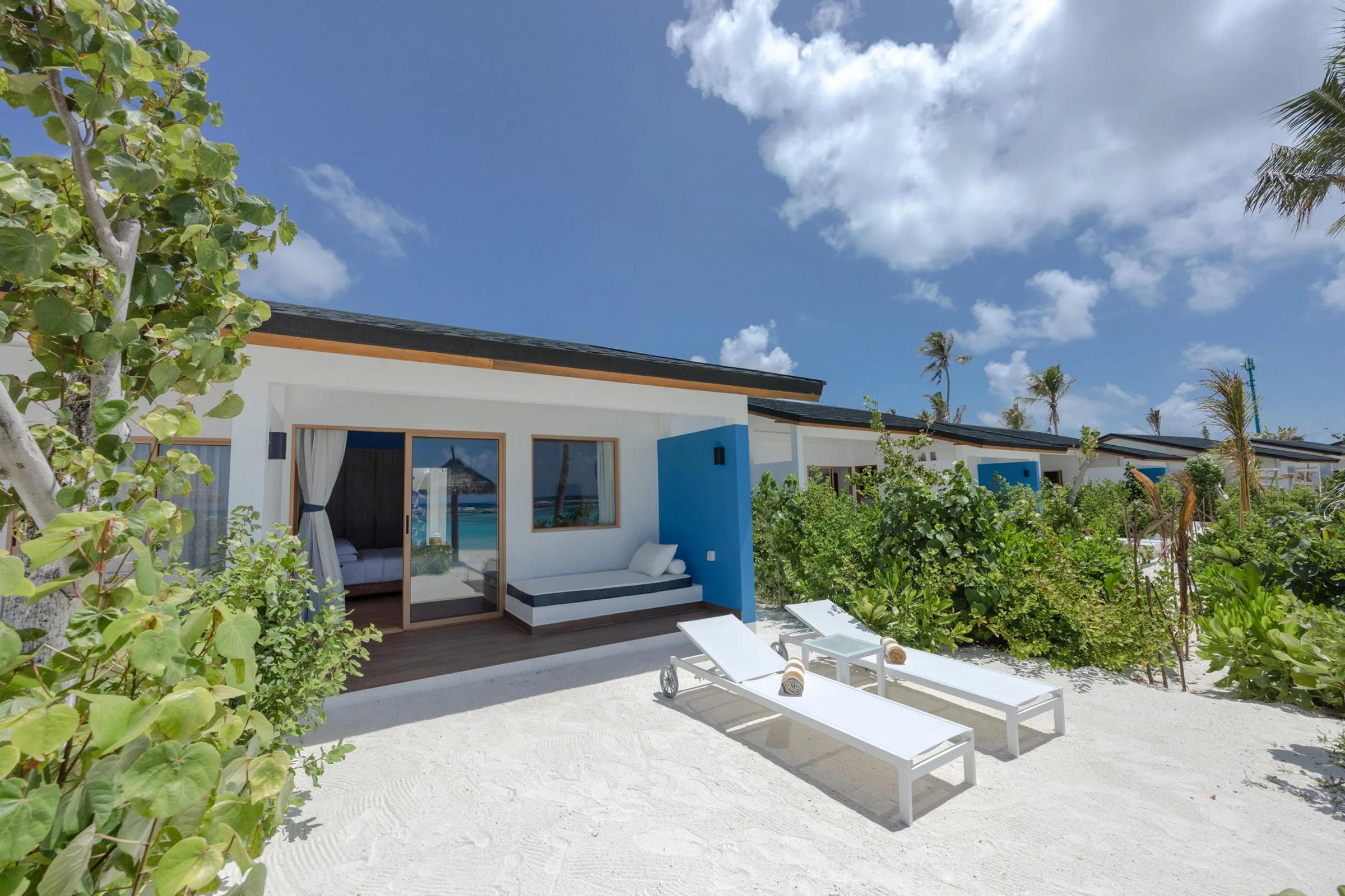 A Beach Villa's exterior deck with sun loungers, glimpsed through sliding doors to the bedroom and lagoon beyond