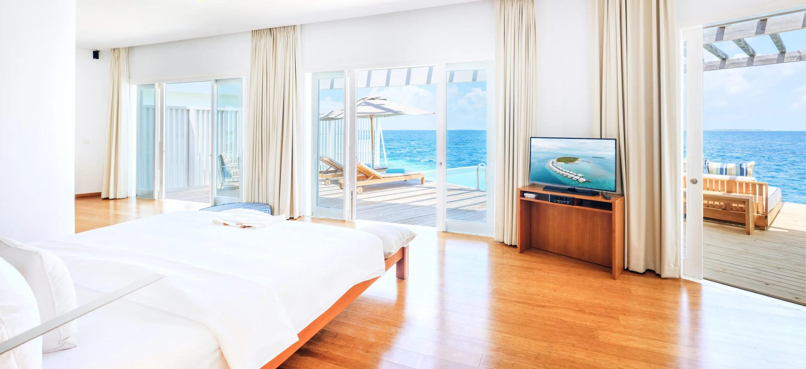 The bedroom of a Reef Water Pool Villa at Amilla, opening onto its private overwater deck and infinity pool