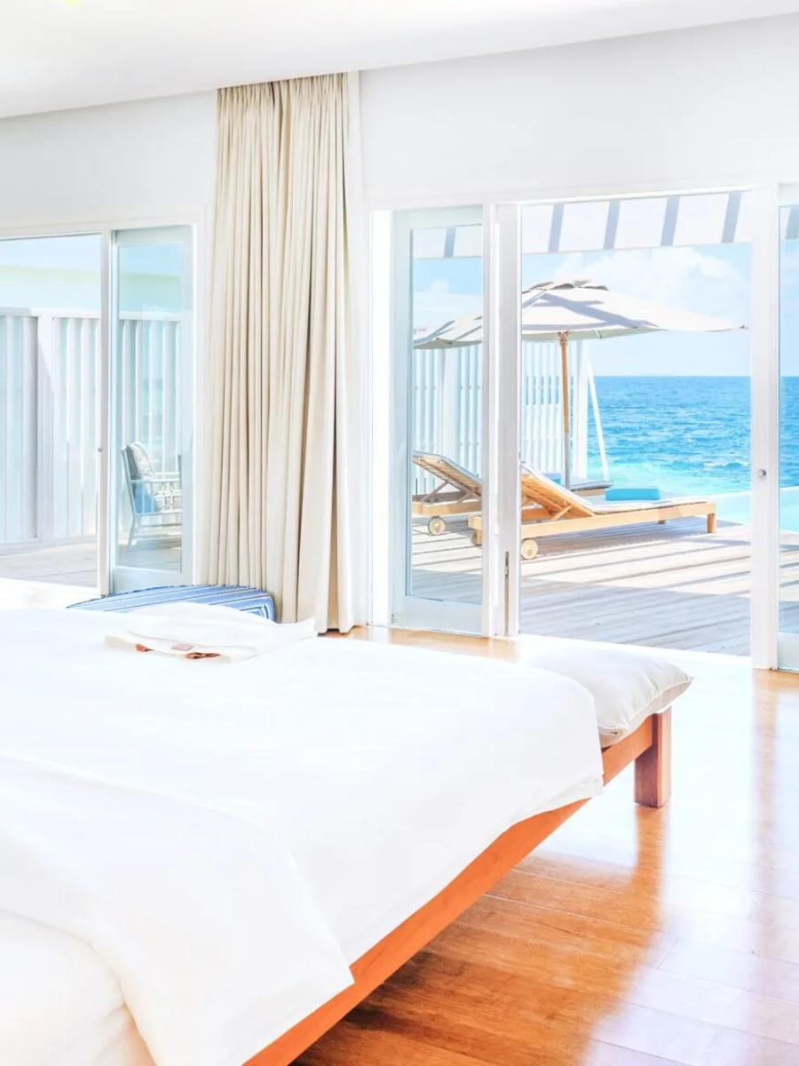 The bedroom of a Reef Water Pool Villa at Amilla, opening onto its private overwater deck and infinity pool
