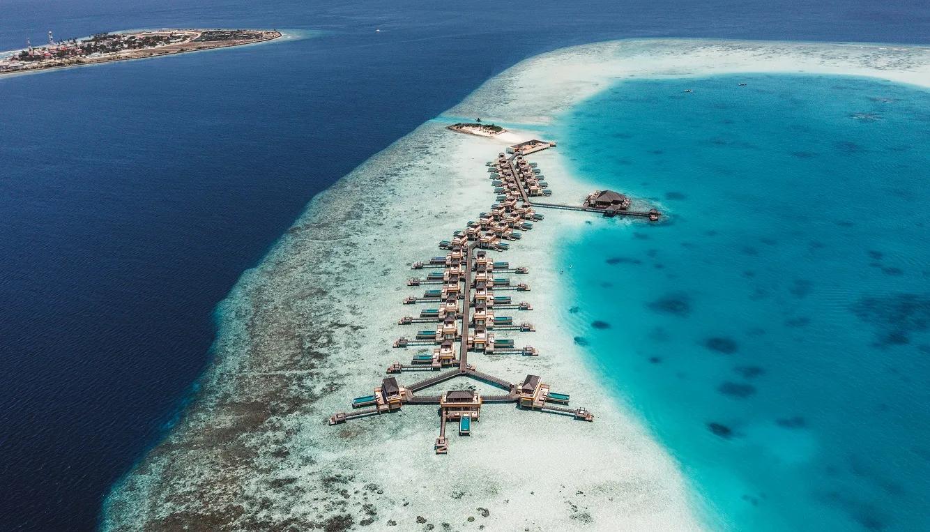Aerial view of a cluster of In-Ocean Pool Villas reaching out from Angsana Velavaru over the lagoon