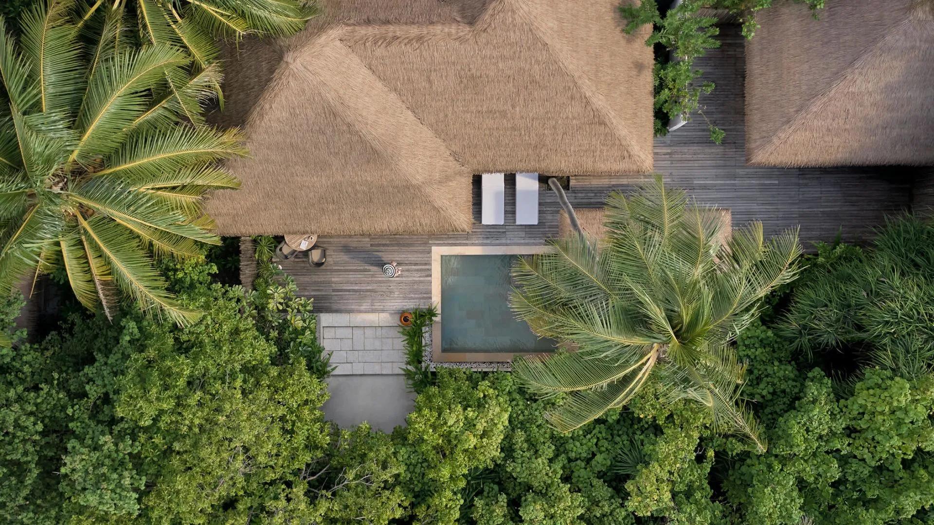 Aerial view directly above a Beach Villa's thatched roof, private pool and sun terrace, framed by palm trees