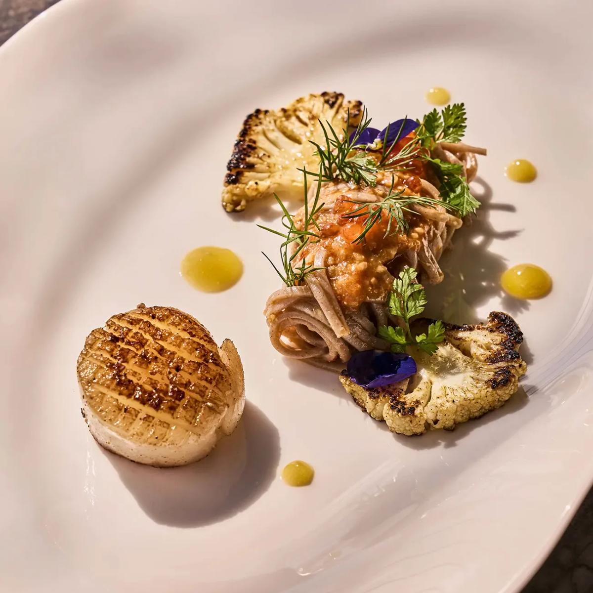 A plated dish from SAFAR Restaurant's Josper-grill menu at .Here, seared scallop with buckwheat noodles and charred cauliflower