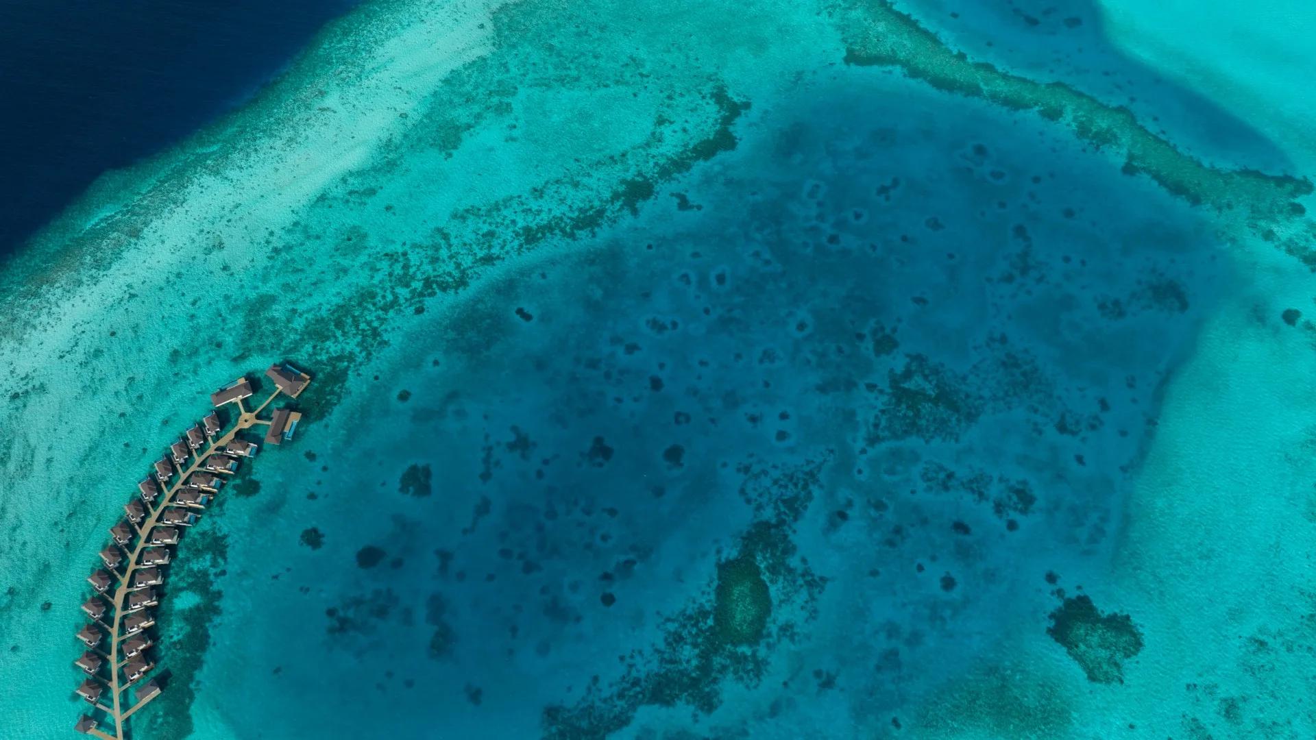 Aerial view of Avani+ Fares Maldives Resort's overwater villas curving along the reef edge, Baa Atoll's turquoise lagoon beyond