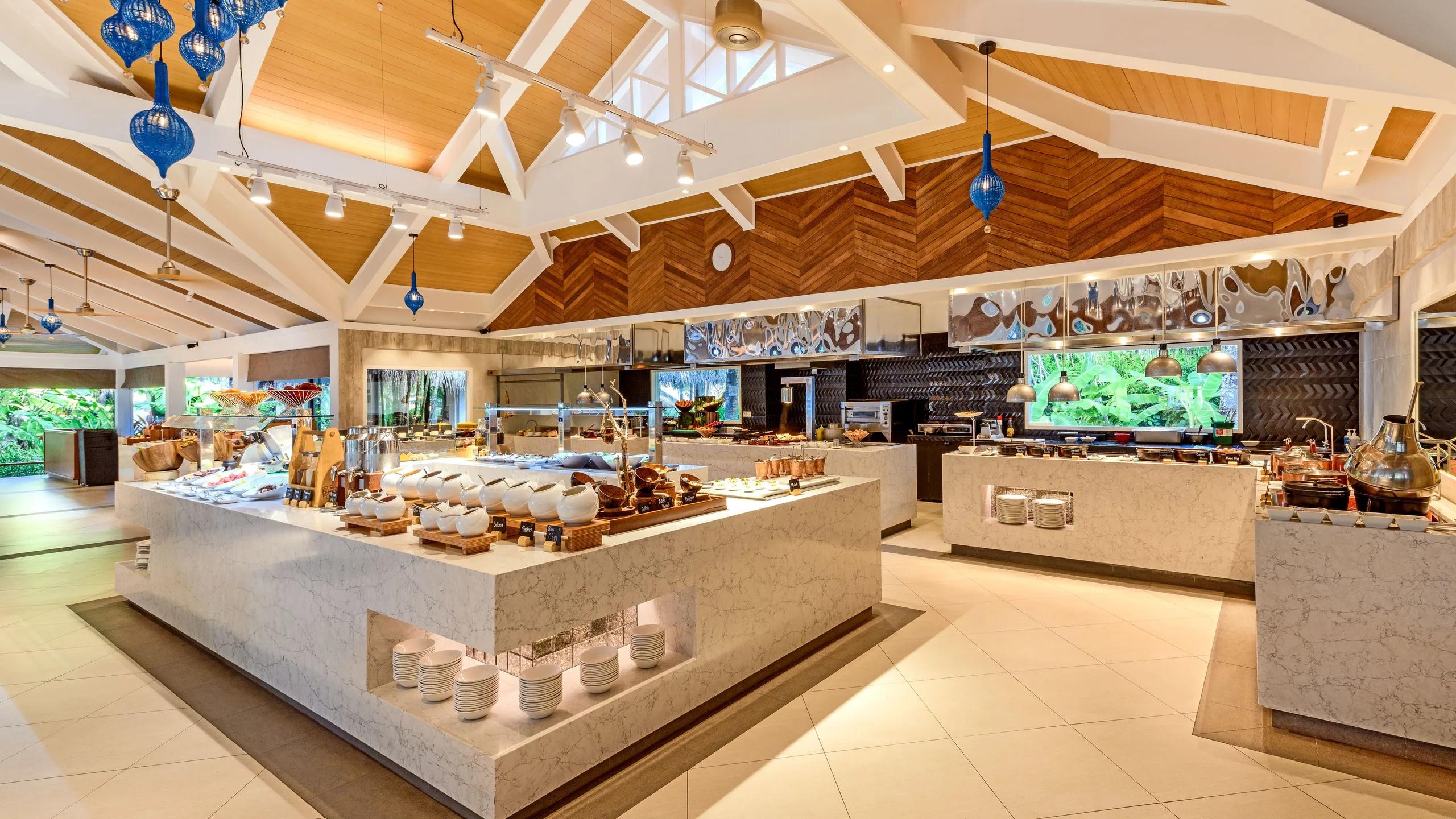 Feast's buffet hall, with marble-topped counters and blue glass pendant lighting under a vaulted timber ceiling