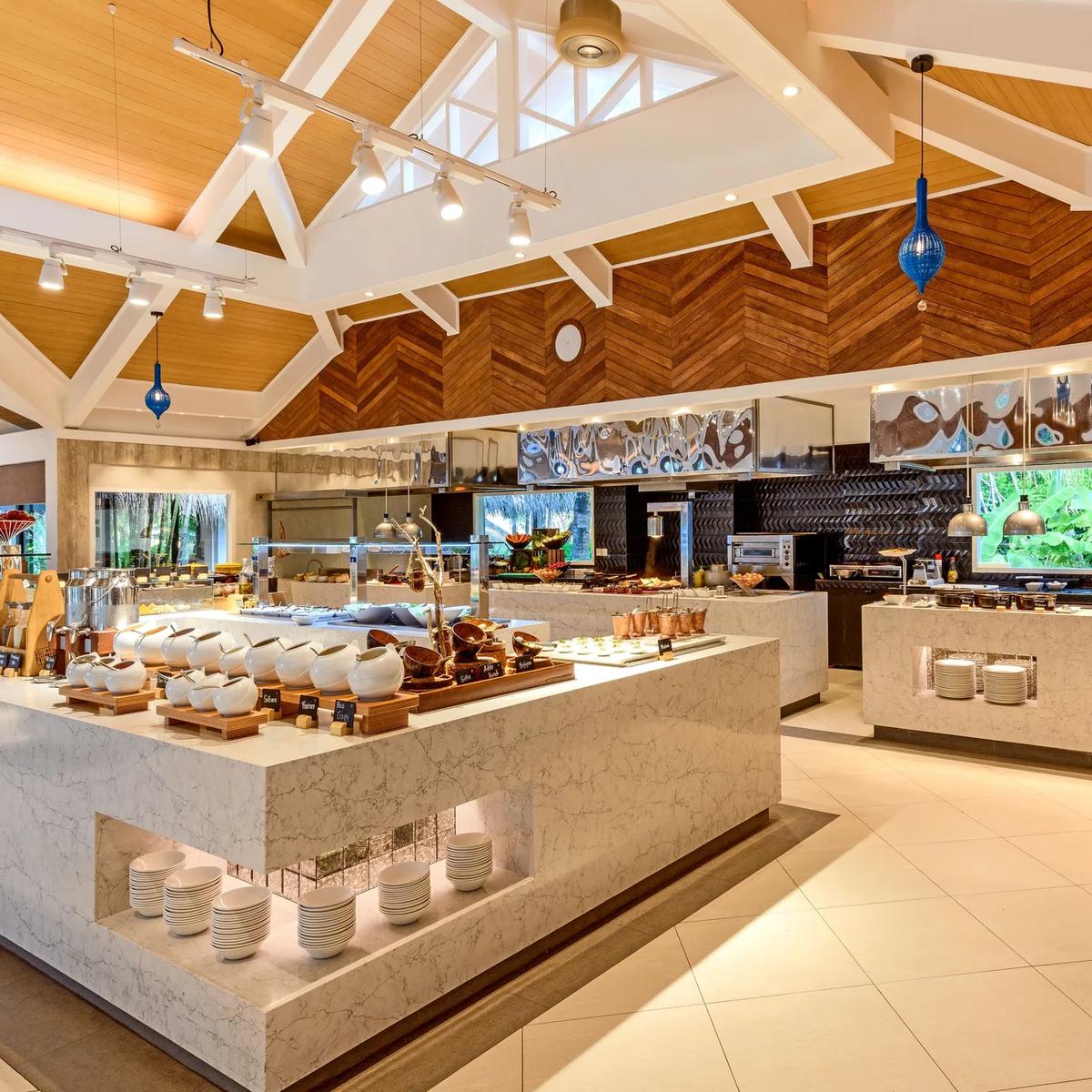 Feast's buffet hall, with marble-topped counters and blue glass pendant lighting under a vaulted timber ceiling