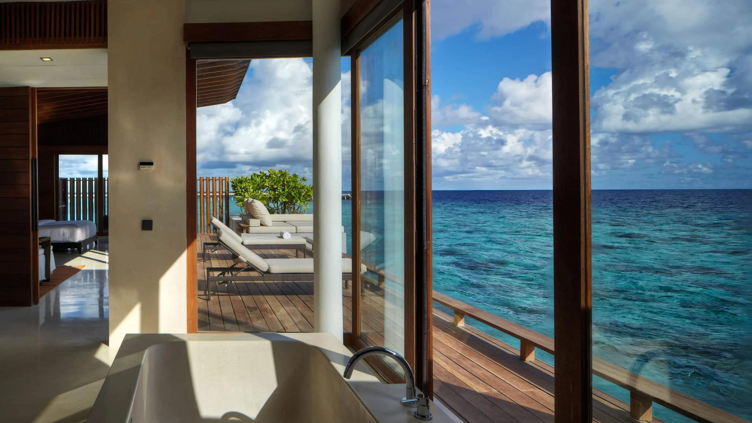 The bathroom of an Overwater Villa, its glass doors sliding open onto the private deck and lagoon