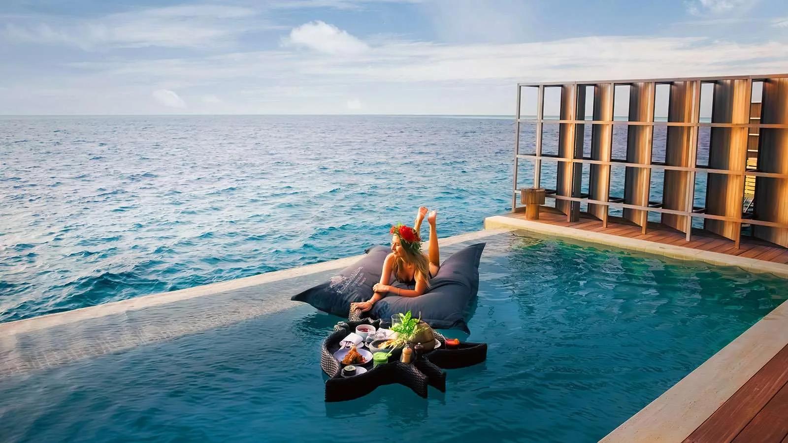 A floating breakfast tray anchored in an Ocean Residence's pool, a guest reclining on cushions beside it