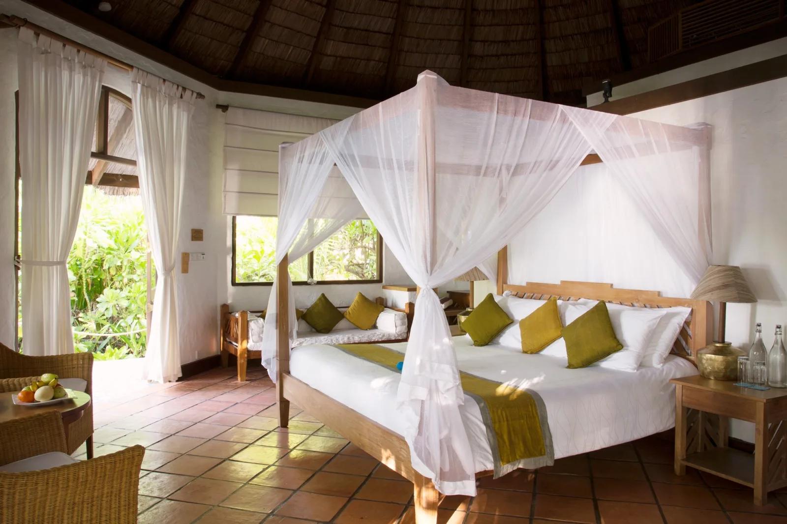 A canopied king bed inside a Deluxe Villa, terracotta tile floor and garden light through open doors