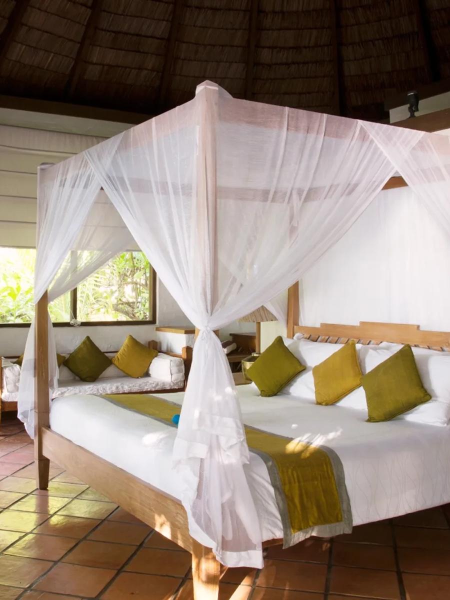 A canopied king bed inside a Deluxe Villa, terracotta tile floor and garden light through open doors