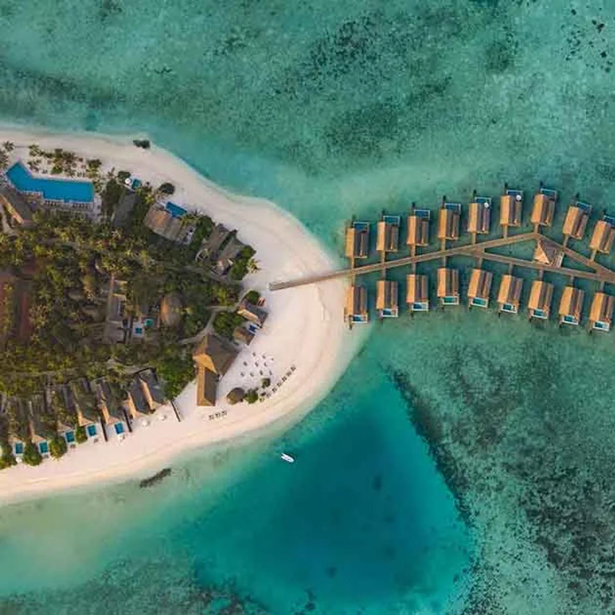 An aerial view of Emerald Faarufushi Resort & Spa's private island in Raa Atoll, overwater villa jetties reaching into the lagoon