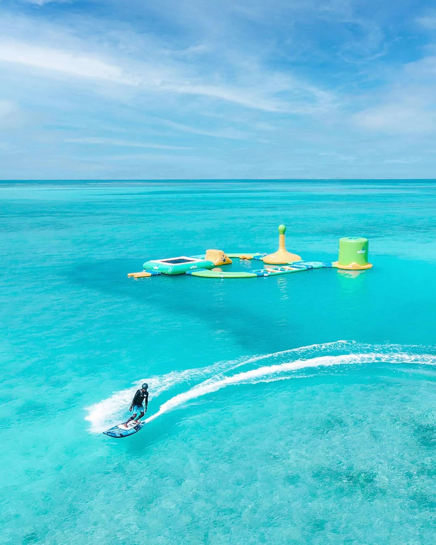 A guest riding a motorised e-surfboard past Hideaway's floating aqua park in the lagoon