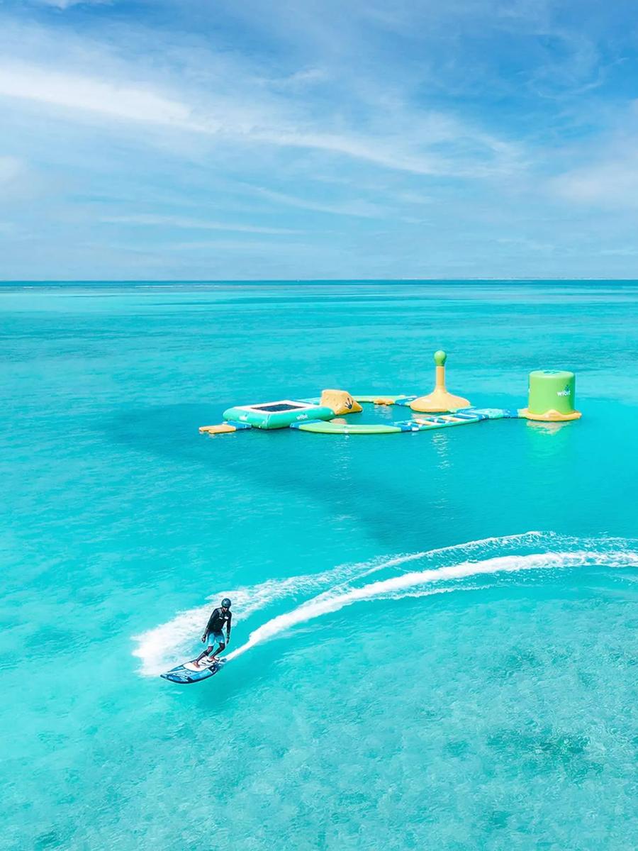 A guest riding a motorised e-surfboard past Hideaway's floating aqua park in the lagoon