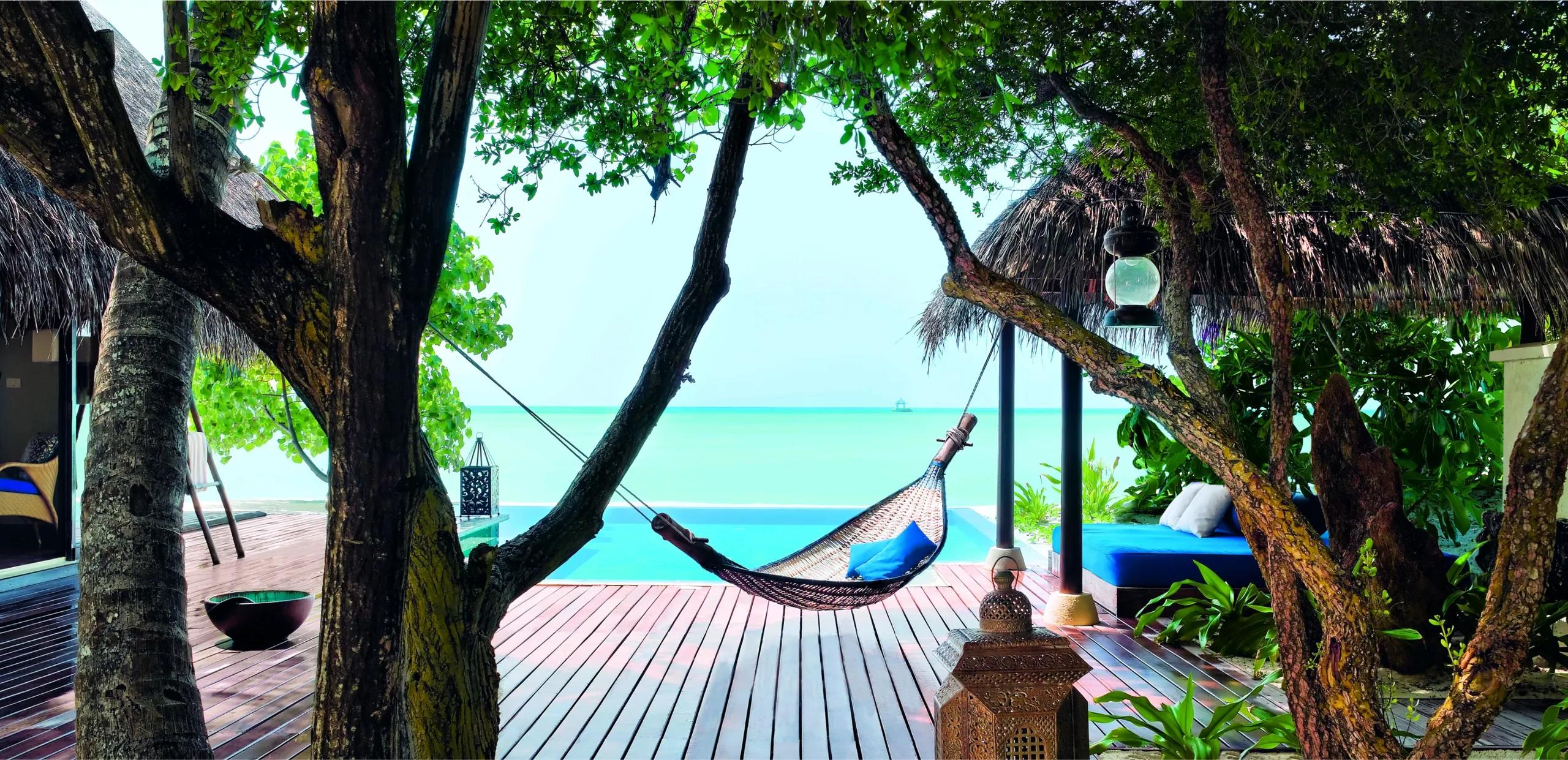 A villa's private plunge pool and deck beneath the trees, a hammock strung between the trunks framing the lagoon beyond