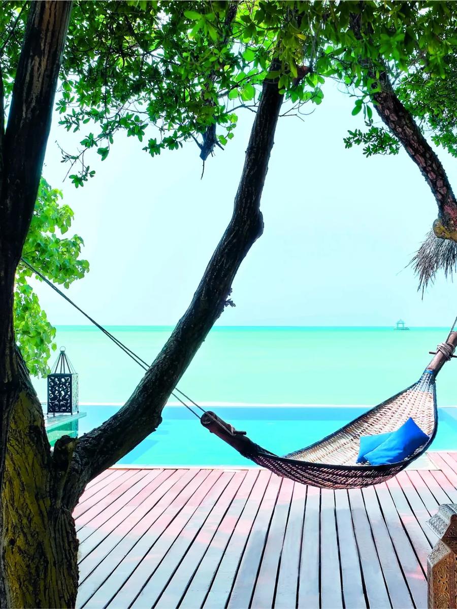 A villa's private plunge pool and deck beneath the trees, a hammock strung between the trunks framing the lagoon beyond