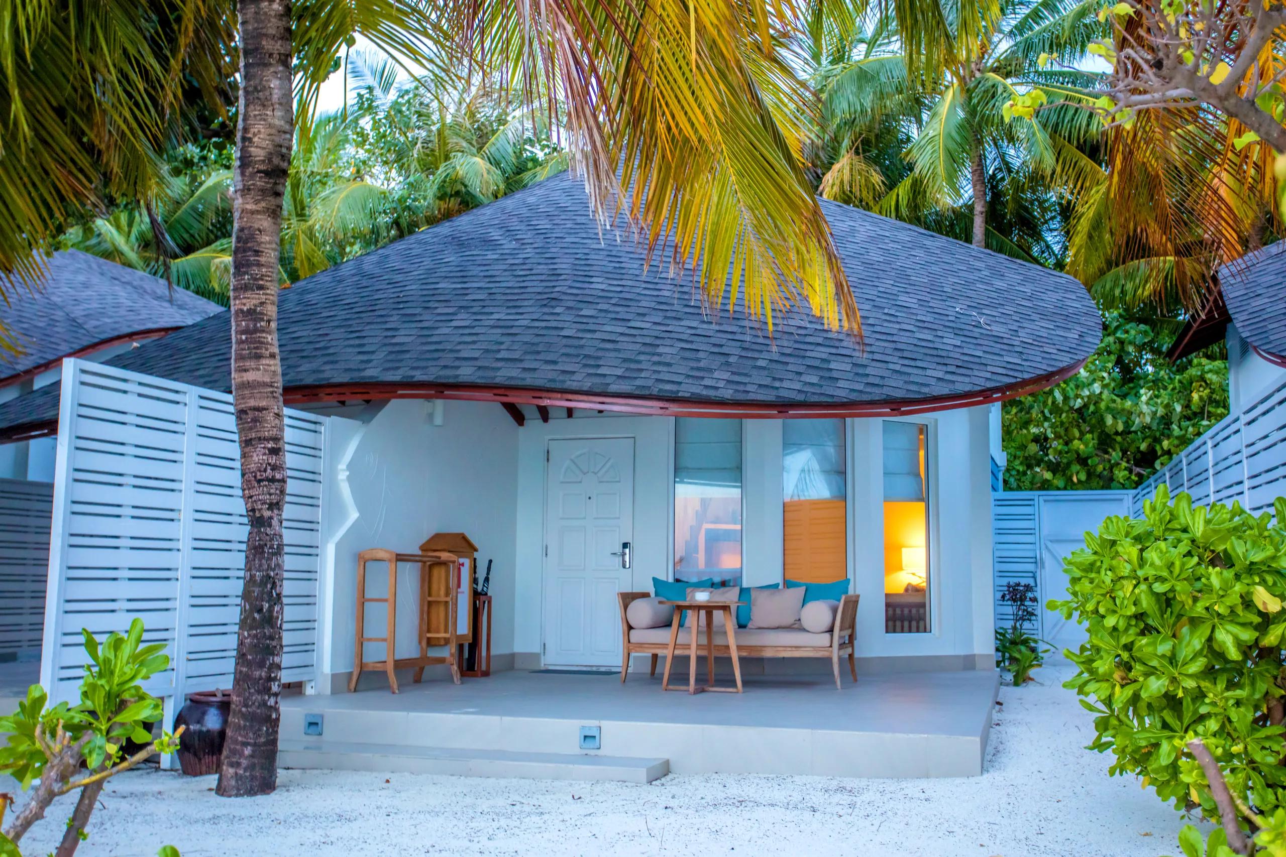 A Duplex Beach Villa's shingled roof and terrace, framed by coconut palms at dusk