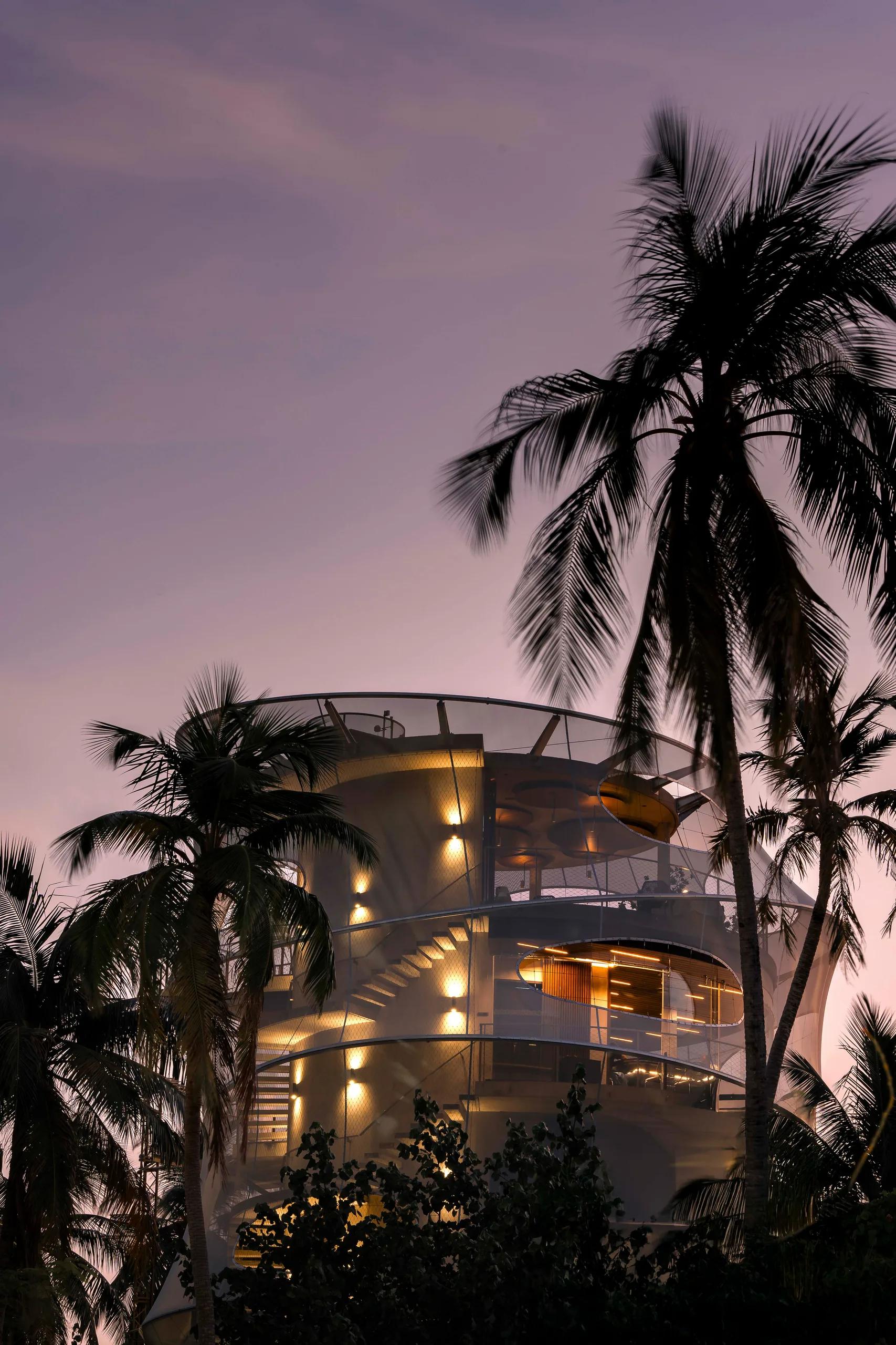 The spiral tower housing Tavaru's teppanyaki dining and wine cellar, lit at dusk and framed by palm trees