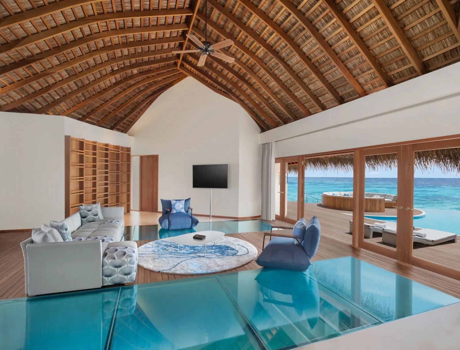 The living area of an overwater villa at W Maldives, with a glass floor panel over the lagoon and a round daybed on the deck outside — representative of the Supreme Overwater category; a dedicated photograph was not available