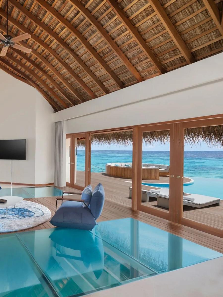 The living area of an overwater villa at W Maldives, with a glass floor panel over the lagoon and a round daybed on the deck outside — representative of the Supreme Overwater category; a dedicated photograph was not available