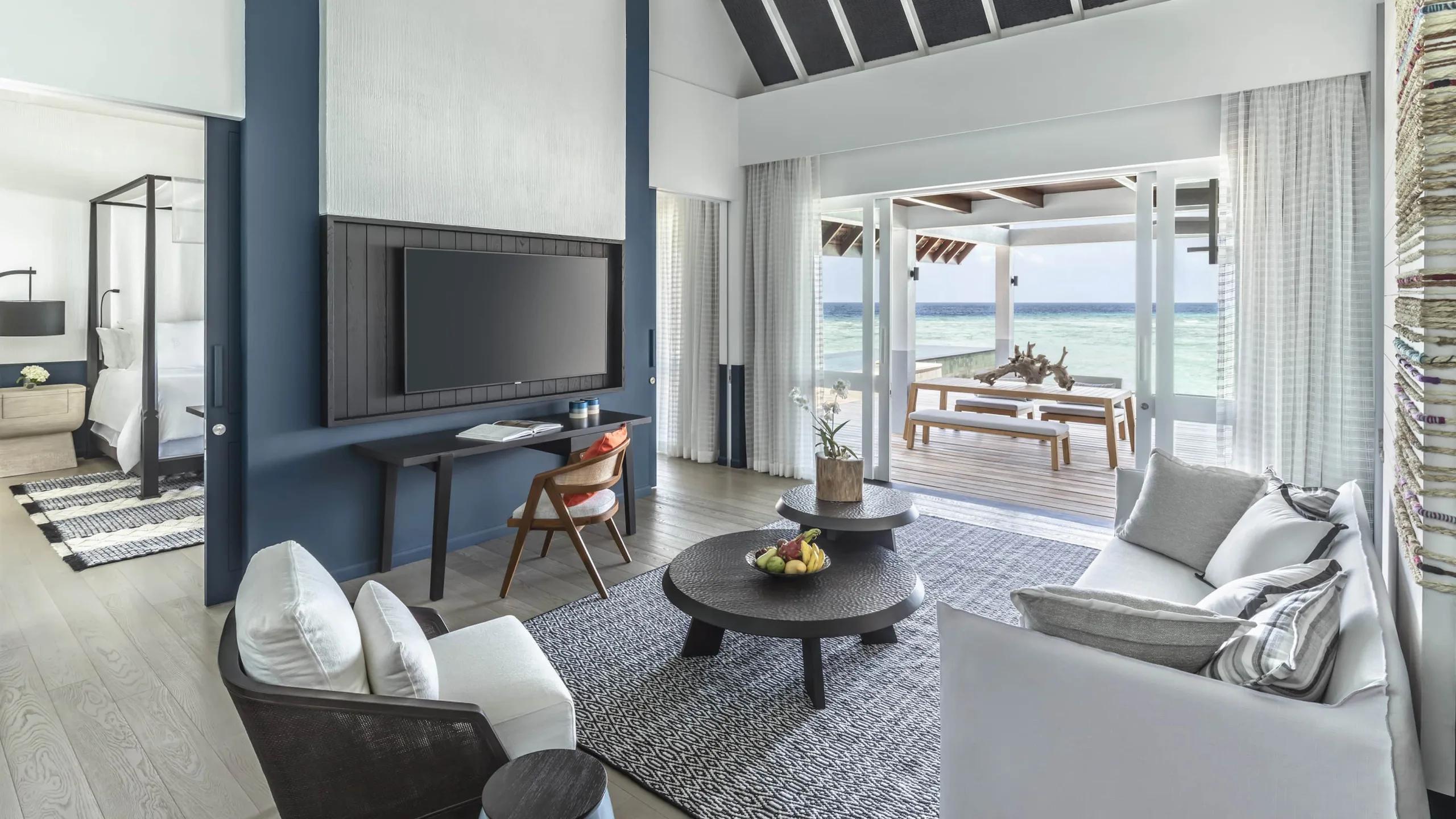 The living area of a Sunset Family Water Villa opening onto its overwater deck and dining table
