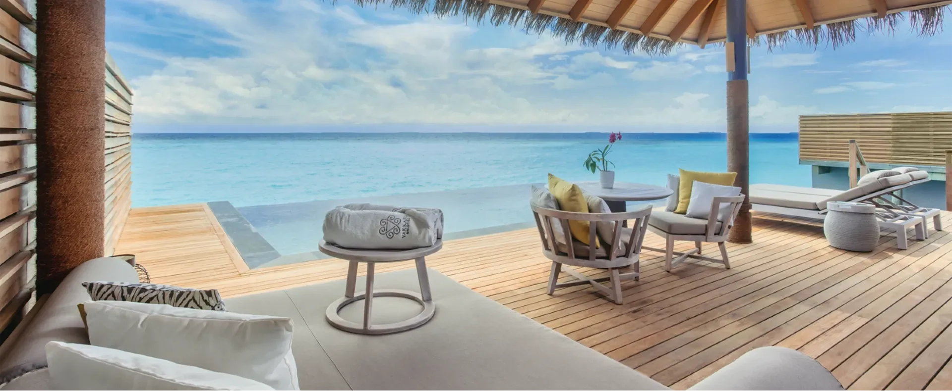 The deck of an Over Water Pool Villa, daybed and lounge chairs beside an infinity-edge pool facing open lagoon