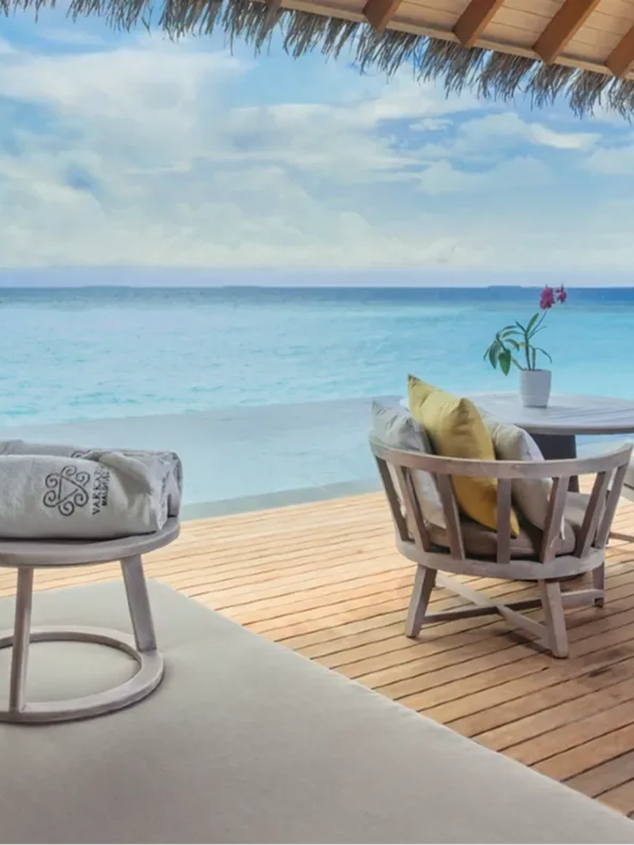 The deck of an Over Water Pool Villa, daybed and lounge chairs beside an infinity-edge pool facing open lagoon