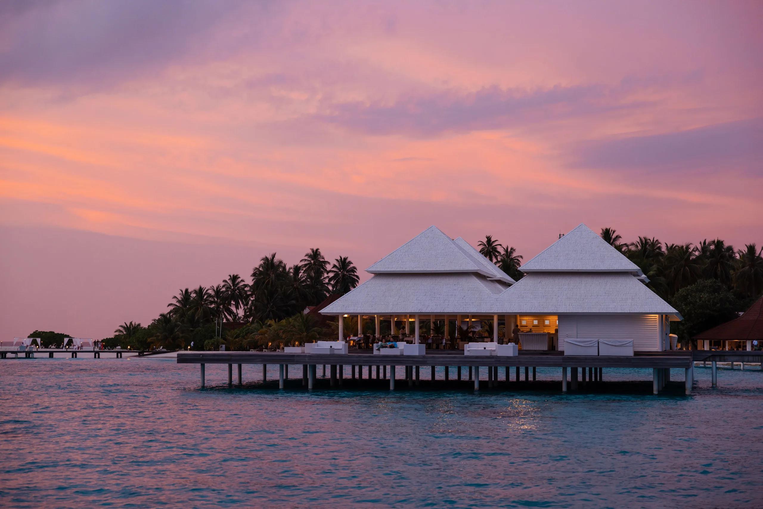 Aqua Over Water Restaurant and Bar lit up at dusk under a pink sky, its jetty stretching back to the island