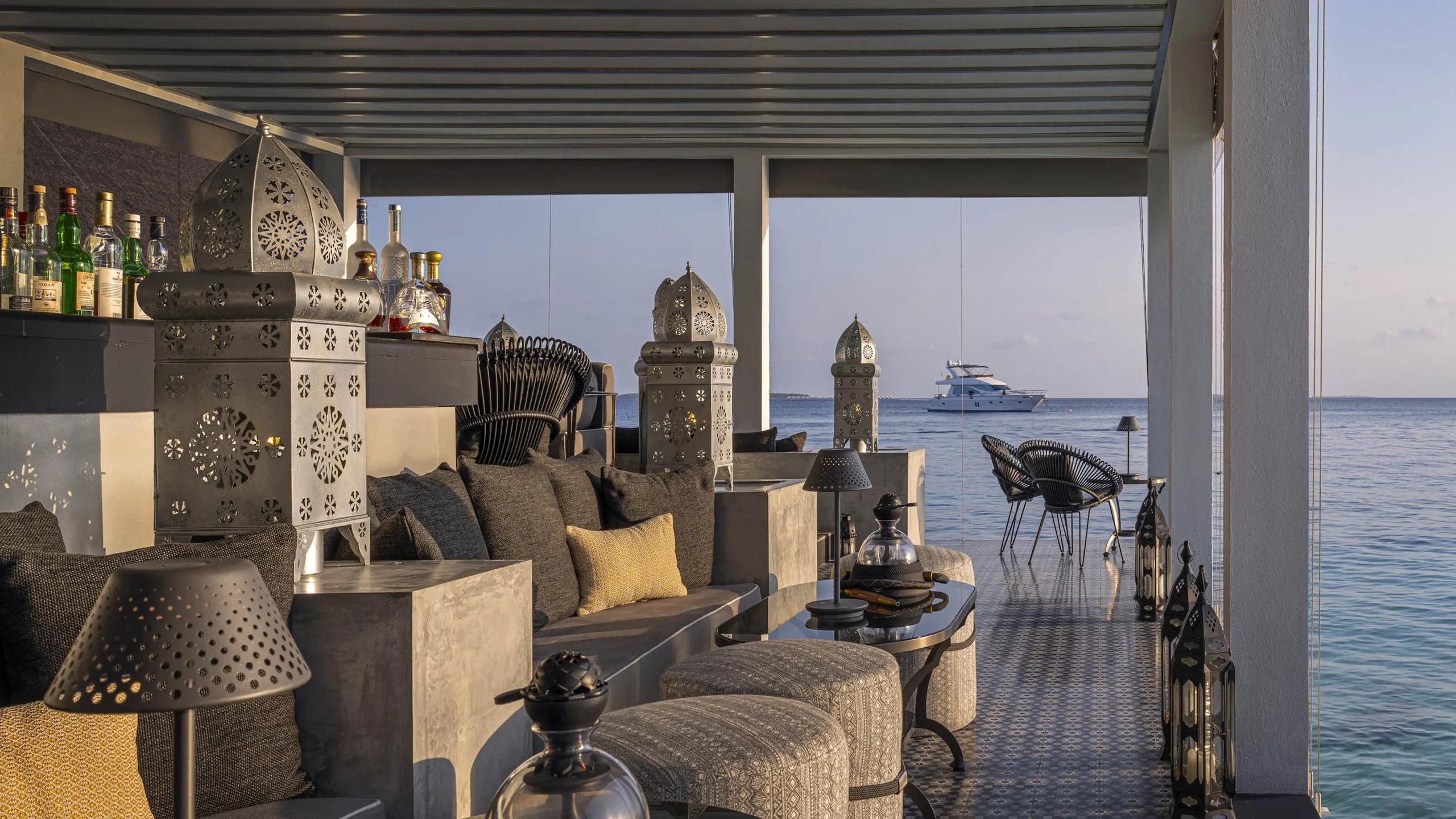 Shisha Bar's overwater lounge with ornate metal lanterns, low seating, and a yacht anchored offshore