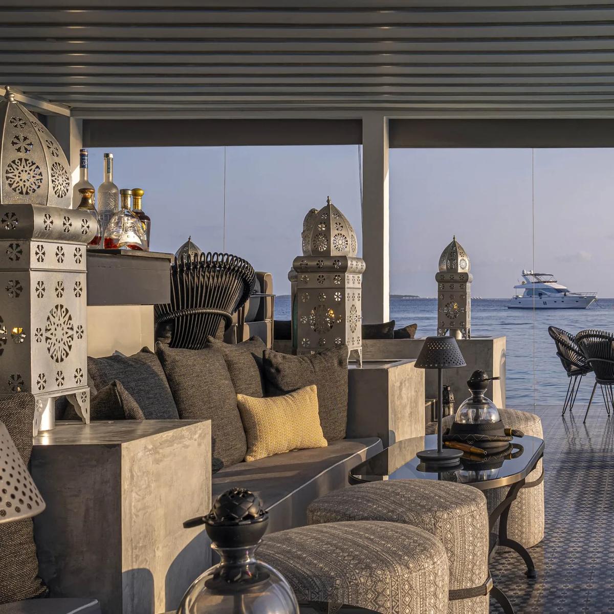 Shisha Bar's overwater lounge with ornate metal lanterns, low seating, and a yacht anchored offshore