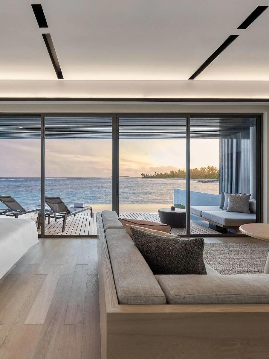 A Sunset Overwater Pool Villa's bedroom lit by the setting sun through floor-to-ceiling glass