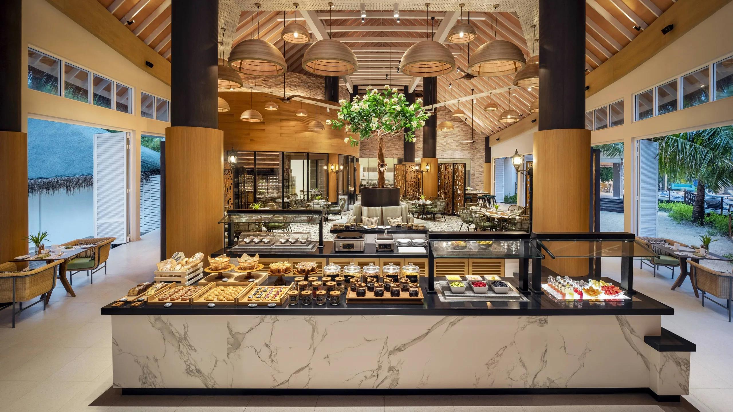The breakfast buffet spread at Aailaa, under a high wood-beamed ceiling with a live tree at its centre