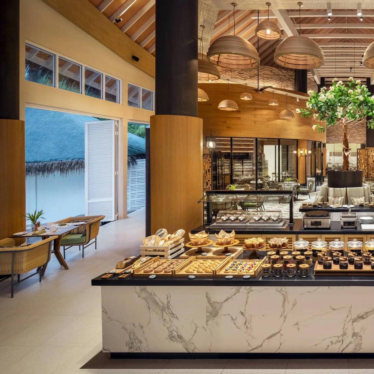 The breakfast buffet spread at Aailaa, under a high wood-beamed ceiling with a live tree at its centre