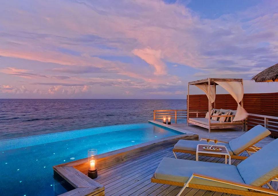A Water Pool Villa's private infinity pool at dusk, deck lanterns lit and open ocean stretching to the horizon