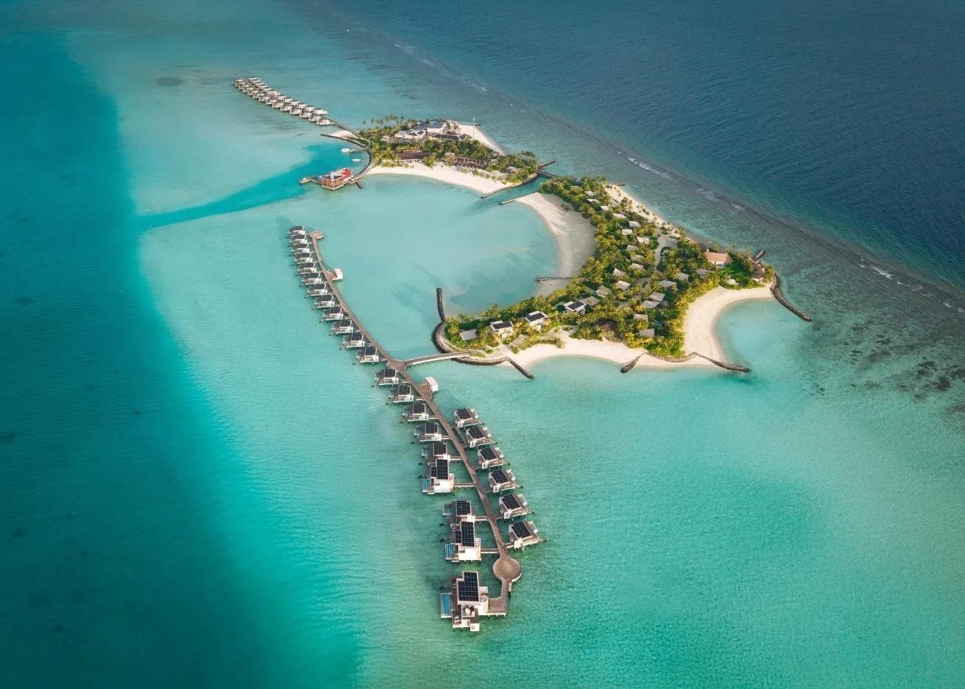 Aerial view of SO/ Maldives' island in Emboodhoo Lagoon, its two rows of overwater villas reaching out from either side of the island and the reef's edge tracing the horizon beyond